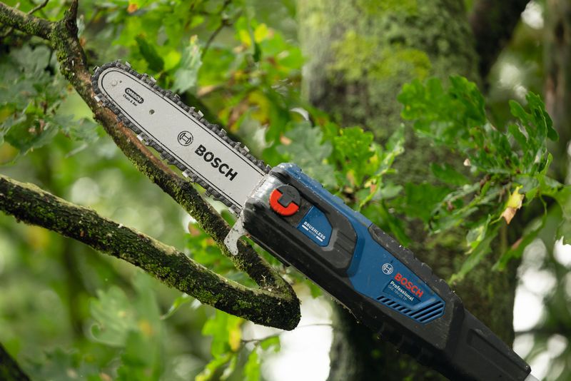 Podadora telescópica inalámbrica que corta la rama de un árbol en un entorno frondoso al aire libre.