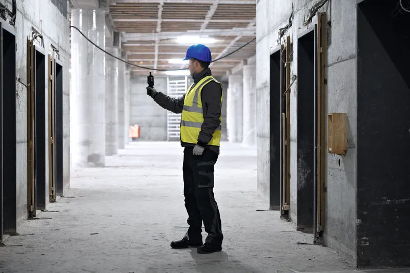 Una persona que usa equipo de seguridad revisa un termohigrómetro dentro de un sitio de construcción.