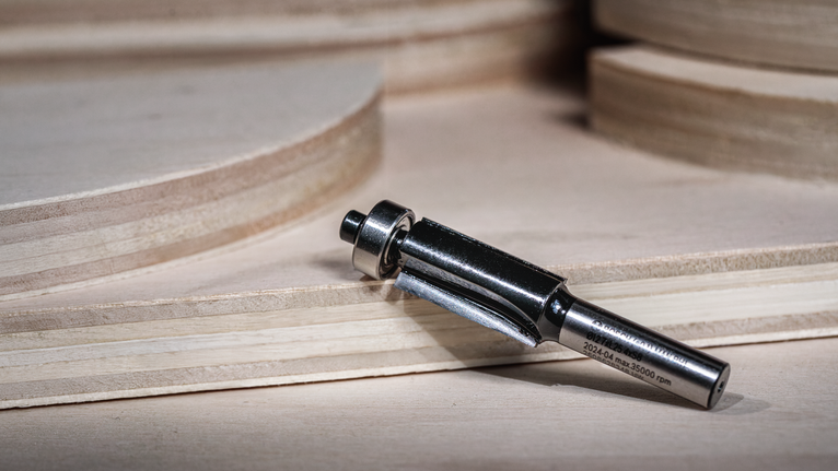 Broca de enrutador colocada sobre una superficie de madera cerca de láminas de madera contrachapada apiladas.