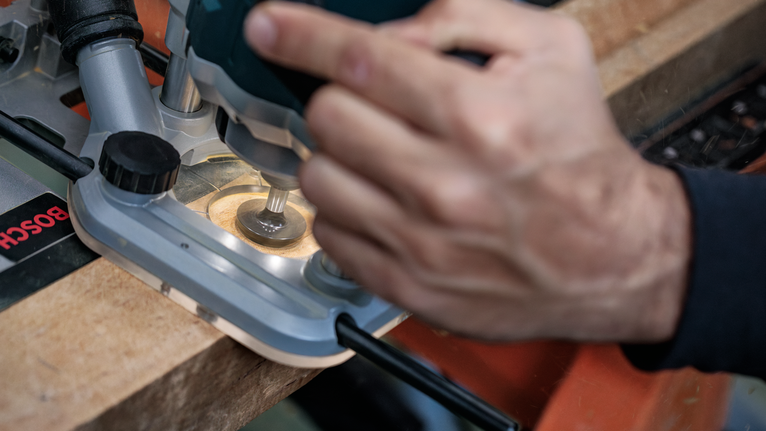 Persona que utiliza una fresadora para dar forma al borde de una tabla de madera.