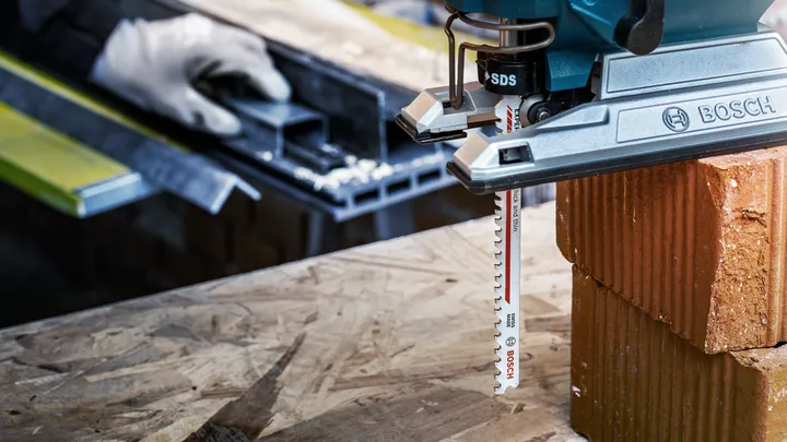 Una persona que usa equipo de seguridad utiliza una sierra caladora para cortar un ladrillo sobre una superficie de madera.