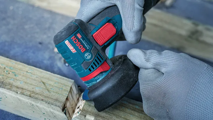 Una persona que usa equipo de seguridad utiliza una amoladora angular para lijar una superficie de madera.