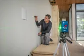 Una persona marca una pared utilizando un nivel láser que proyecta líneas verdes.