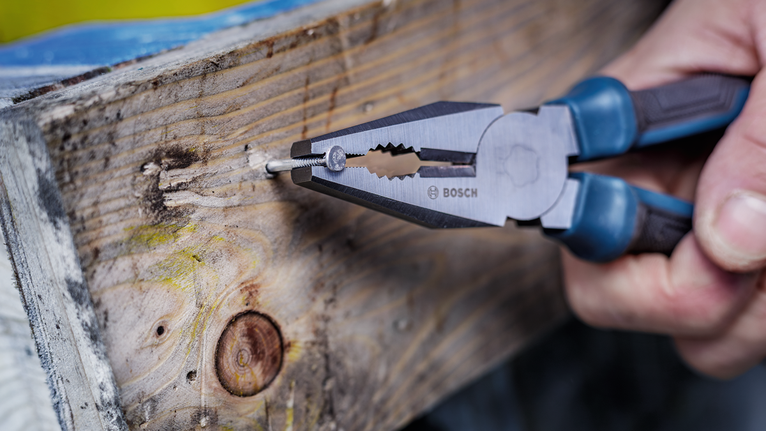 Una persona utiliza unos alicates para sujetar un clavo en una tabla de madera.