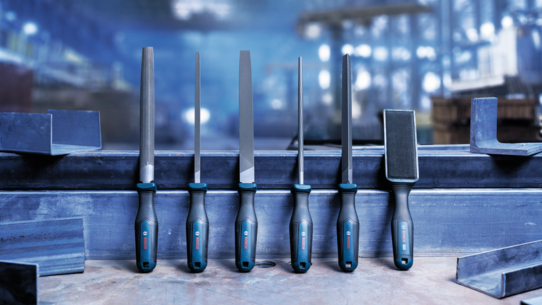 En un taller, seis limas metálicas con mangos negros y azules están dispuestas verticalmente sobre una viga metálica.