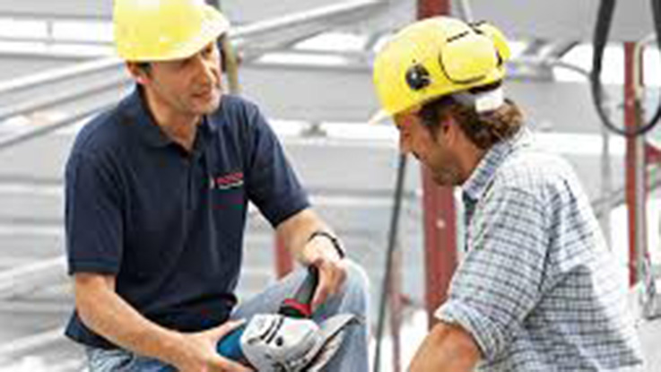 Dos hombres con cascos amarillos revisan una herramienta Bosch en un sitio de construcción.