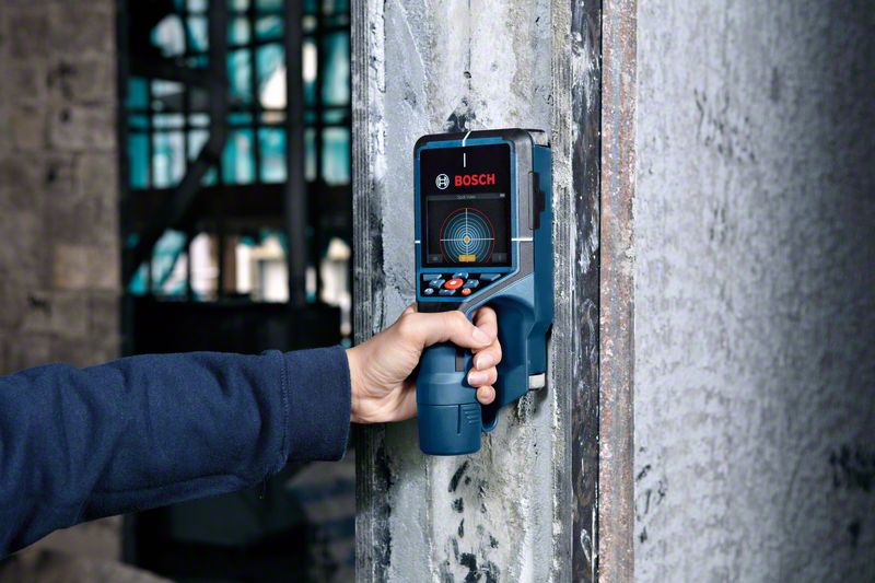 Una persona sostiene un detector Bosch contra una pared de cemento.