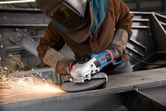 Osoba v bezpečnostním vybavení brousí kov úhlovou bruskou a vytváří jiskry.