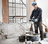 Osoba v bezpečnostním vybavení míchá stavební materiál míchacím mechanismem.