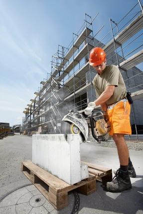 Osoba v bezpečnostním vybavení řeže velký betonový blok motorovou pilou.
