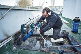 Osoba v bezpečnostním vybavení vrtá do betonu diamantovou vrtačkou namontovanou na zdi.