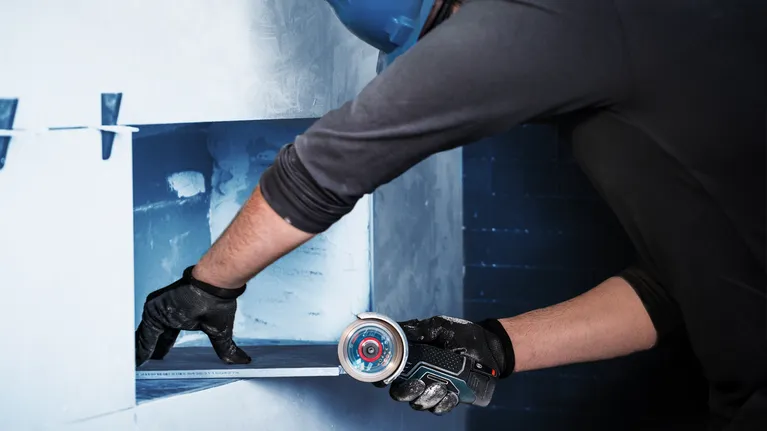 Osoba v bezpečnostním vybavení vyřezává otvor ve zdi kompaktním elektrickým nářadím.