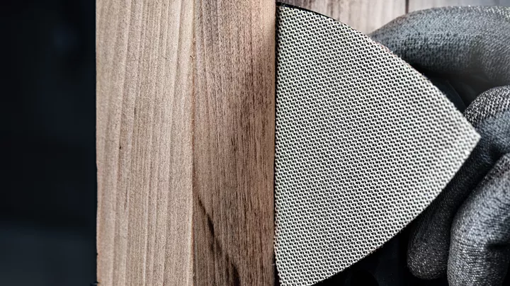 Osoba v bezpečnostním vybavení brousí dřevěný povrch brusným kotoučem se síťovinou.