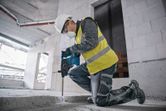 Osoba v bezpečnostním vybavení používá vrtací kladivo k rozbíjení betonu na staveništi.