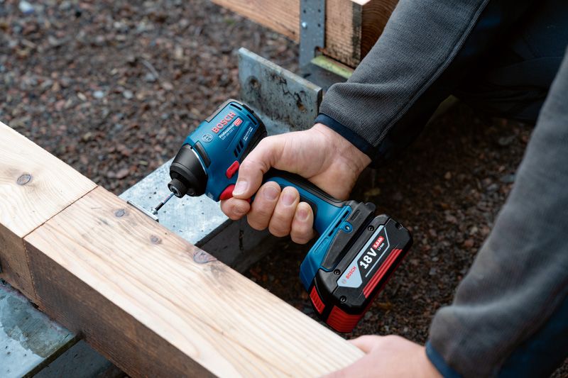 Osoba používá akumulátorovou vrtačku k zašroubování šroubu do dřevěných trámů.