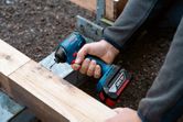 Osoba používá akumulátorovou vrtačku k zašroubování šroubu do dřevěných trámů.