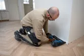 Osoba v bezpečnostním vybavení používá akumulátorovou hřebíkovačku na dřevo k instalaci podlahových obkladů.