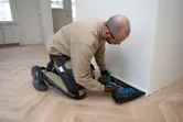 Osoba v bezpečnostním vybavení používá akumulátorovou hřebíkovačku k instalaci podlahových obkladů.