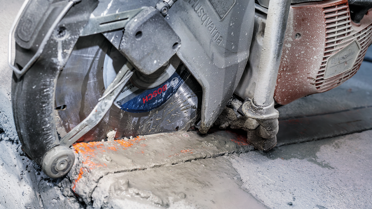 Pila na beton řeže cementový povrch s viditelným prachem a kalem.
