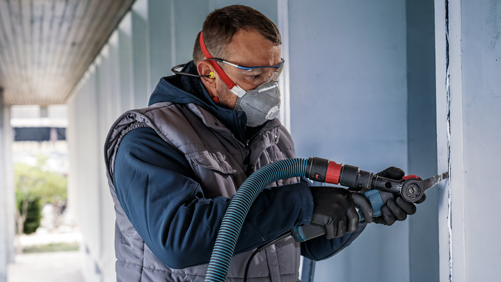 Osoba v bezpečnostním vybavení řeže zeď elektrickým nářadím.