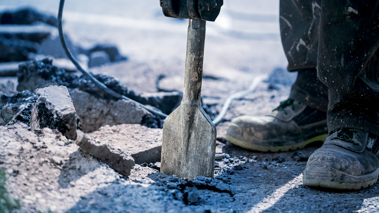 Osoba v bezpečnostním vybavení rozbíjí beton demoliční nářadí.