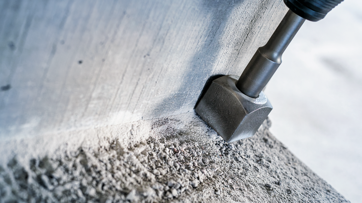 Rotační kladivo sekáč láme beton podél zdi.