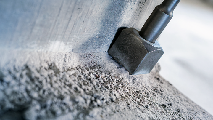 Sekáč láme beton na drsném povrchu stavby.