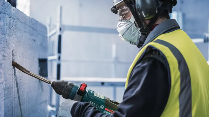 Osoba v bezpečnostním vybavení seká beton elektrickým nářadím.