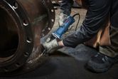 Osoba v bezpečnostním vybavení používá přímou brusku na kovové přírubě.