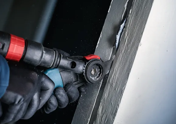 Osoba v bezpečnostním vybavení používá elektrické nářadí k řezání do natřeného povrchu.