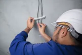 Osoba v bezpečnostním vybavení upevňuje elektrické kabely ke stropu.