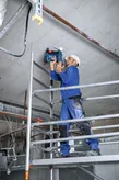 Osoba v bezpečnostním vybavení používá akumulátorovou hřebíkovačku na beton na stropě.