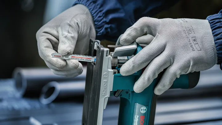 Osoba v bezpečnostním vybavení vkládá pilový kotouč do elektrického nářadí.