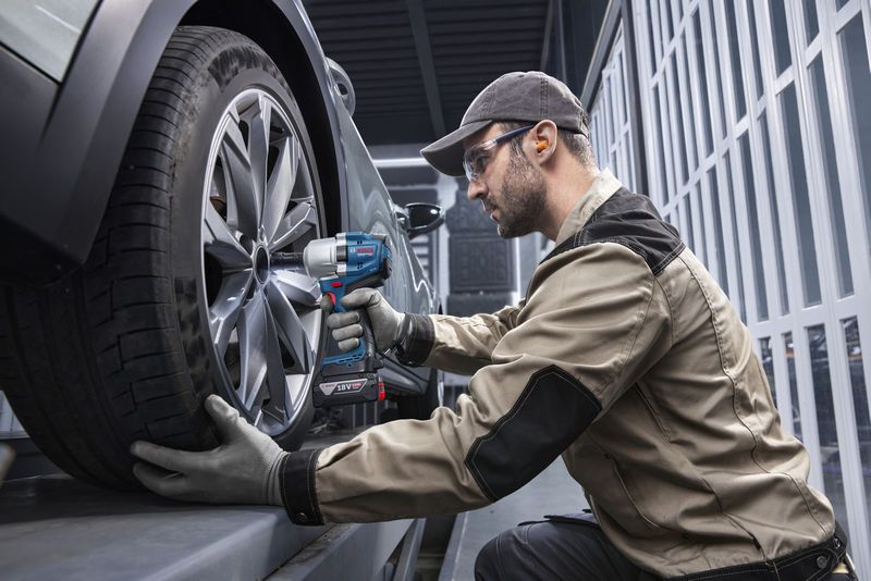 Osoba v bezpečnostním vybavení používá akumulátorový rázový utahovák k utažení kola automobilu.