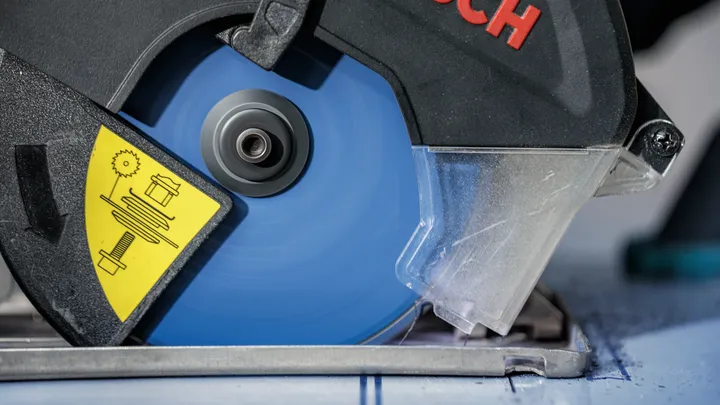 Kotoučová pila s modrým kotoučem řeže označený kus materiálu.