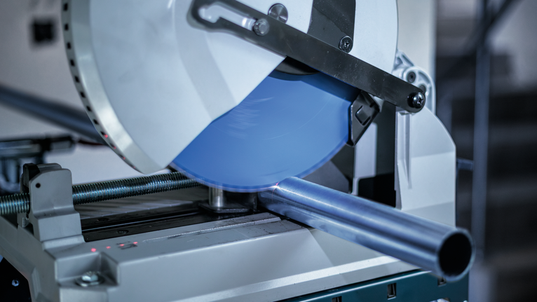 Řezací pila na kov řezající ocelovou trubku v dílně.