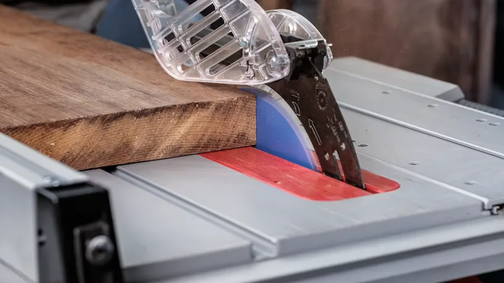 Kotoučová pila řeže dřevěnou desku s nasazeným bezpečnostním krytem.