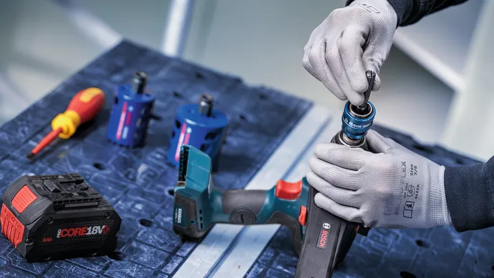 Osoba v bezpečnostním vybavení připevňuje vrták k akumulátorovému elektrickému nářadí.