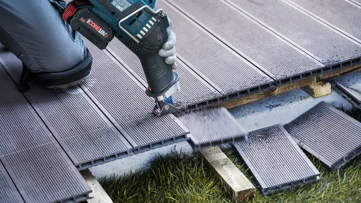 Osoba v bezpečnostním vybavení řeže kompozitní terasy elektrickým nářadím.