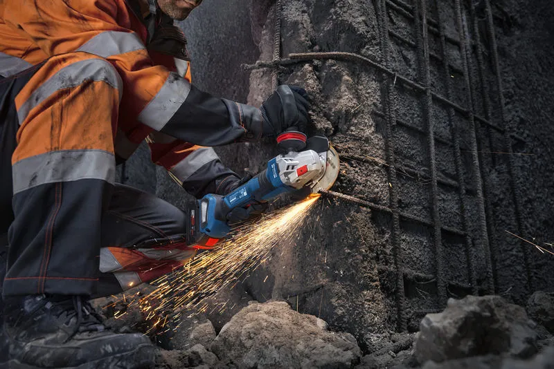 Osoba v bezpečnostním vybavení řeže beton úhlovou bruskou a vytváří jiskry.