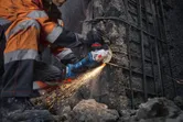 Osoba v bezpečnostním vybavení řeže beton úhlovou bruskou a vytváří jiskry.