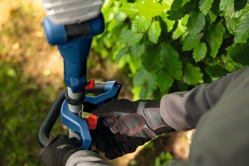 Osoba v bezpečnostním vybavení zastřihuje keře akumulátorovými nůžkami na živý plot.