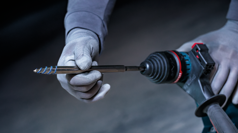 Osoba v bezpečnostním vybavení vkládá vrták do elektrického nářadí.