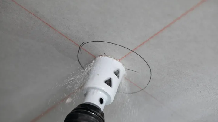 Děrová pila vyřeže kruhový otvor v sádrokartonu, vedená protínajícími se laserovými liniemi.