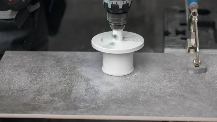 Vrtačka s nástavcem pro děrovou pilu vyřízne kruhový otvor v dlaždicové desce.