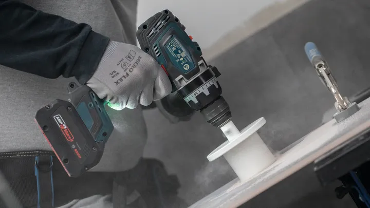 Osoba v bezpečnostním vybavení vyvrtá díru do bílého povrchu.