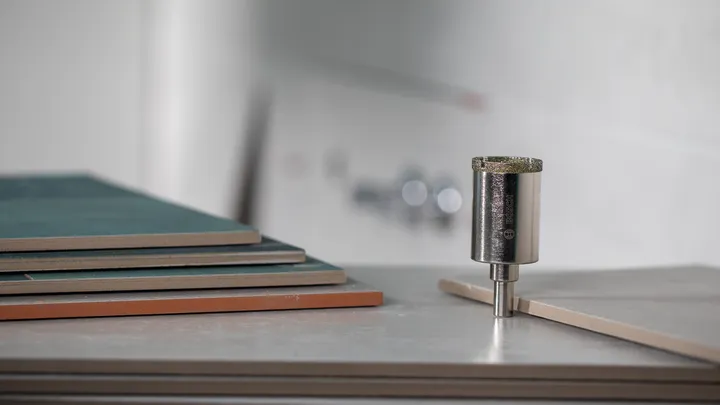 Diamantový jádrový vrták umístěný svisle vedle naskládaných dlaždic.