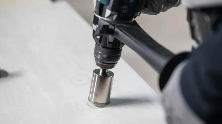 Osoba v bezpečnostním vybavení vyvrtá kruhový otvor do betonového povrchu.