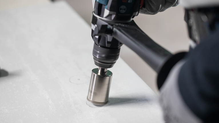 Osoba v bezpečnostním vybavení vyvrtá kruhový otvor do betonového povrchu.