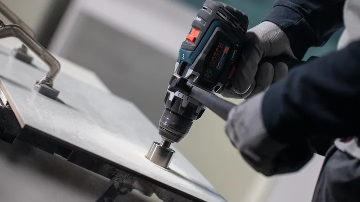 Osoba v bezpečnostním vybavení vyvrtá díru do dlaždicového povrchu.